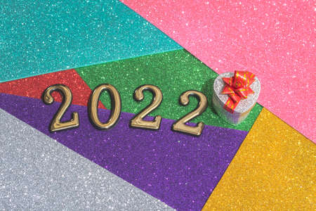 On a colorful bright shiny New Year background, a silver gift box with a red bow and golden numbers 2022. Concept for New Year's card, invitation.の写真素材