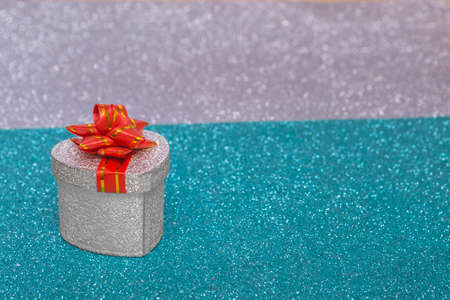 On a colorful bright shiny Christmas background, a silver gift box with a red bow. Concept for New Year's card, invitation. New Year 2022.の写真素材