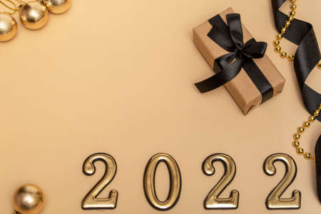 New Year 2022. Top view New Year mockup on beige background: black ribbon, gift box, golden numbers...
