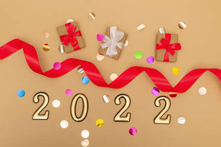 New Year 2022. Top view New Year mockup on beige background: red ribbon, gift box, gold numbers and...