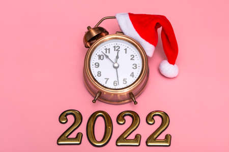 New year concept on pink background alarm clock in santa hat with golden numbers 2022, close upの写真素材