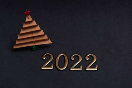 New Year's composition. Brown paper christmas tree with golden numbers 2022 on black background with...