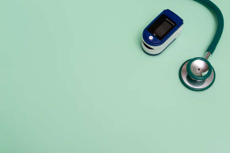Medical flat plan with pulse oximeter and stethoscope on green background. A pulse oximeter used to...