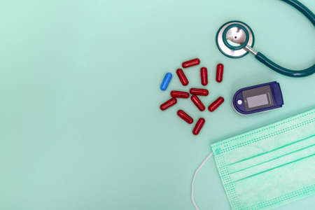 Medical flat lay with pulse oximeter, stethoscope, pills and medical mask on green background. A pulse oximeter used to measure oxygen levels. With copy spaceの写真素材