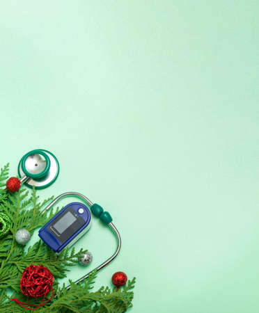 Medical concept: celebrating Christmas in healthcare. Top view of a flat lay close-up of a stethoscope, pulse oximeter with fir branches on a green background. With copy space.Vertical photoの写真素材