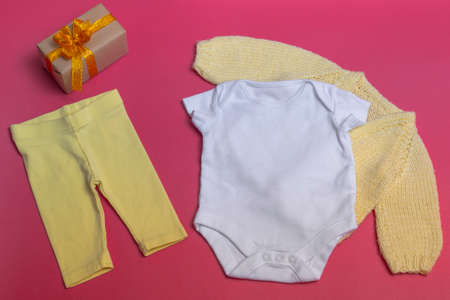 On a colored background, an empty white baby bodysuit close-up - with a knitted yellow jacket and yellow leggings - a mock-up of newborn clothes. With copy spaceの写真素材