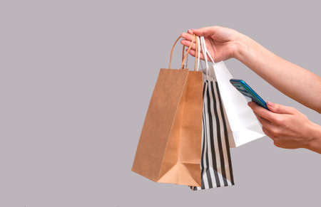 Woman shopping online from a mobile phone. Female hands with packages isolated on gray background, close up copy spaceの写真素材