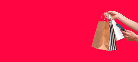 Woman shopping online from a mobile phone. Female hands with packages isolated on red background, close up copy space. Bannerの写真素材