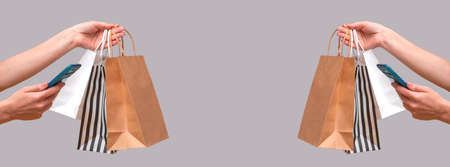 Woman shopping online from a mobile phone. Female hands with packages isolated on gray background, close up copy space. Bannerの写真素材