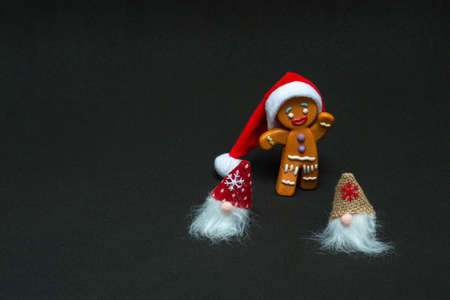 Christmas concept. Gnomes and gingerbread man in santa hat on black background with copy space, close upの写真素材