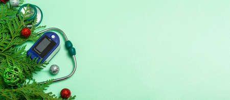 Medical concept: celebrating Christmas in healthcare. Top view of a flat lay close-up of a stethoscope, pulse oximeter with fir branches on a green background. copy spaceの写真素材