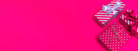 An overhead view of a white gift with pink stripes and white polka dots on a pink background with copy space. Bannerの写真素材
