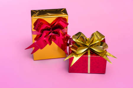 Beautiful golden gift boxes with a red bow on a colored background close up, top viewの写真素材