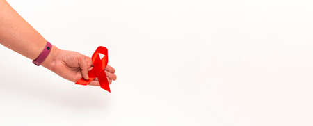 Medical concept for World AIDS Day in December. Red AIDS awareness ribbon clutched in a woman's hand...