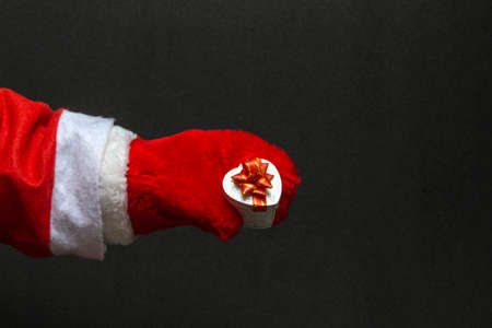 Close-up of Santa Claus in red mittens holding a gift on a black background with copy spaceの写真素材