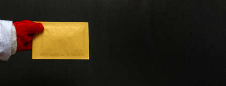 Merry Christmas and Happy New Year concept. Close up on black background santa claus hand holding envelope with copy space. Bannerの写真素材