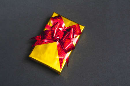Beautiful gift gold box with a red bow on a black background close-up, top view, with copy spaceの写真素材