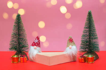Festive concept. On a colored background in lights, a podium for cosmetics and various goods with gnomes, gifts and Christmas trees. Close up, copy spaceの写真素材