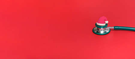 Medical stethoscope in red Santa Claus hat on a red background. With copy space.Bannerの写真素材
