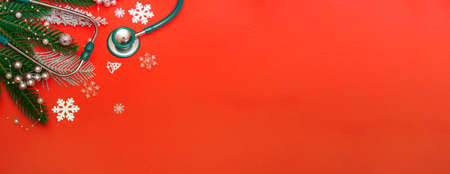Top view of flat Christmas decorations and stethoscope on red background. Concept for medical announcement, banner. With copy spaceの写真素材