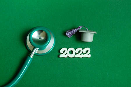 Graduation cap with stethoscope and numbers 2022 on green background, close up with copy space. Medical education concept.の写真素材