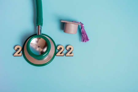 Graduation cap with stethoscope and numbers 2022 on blue background, close up with copy space. Medical education concept.の写真素材