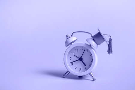 Yellow alarm clock with graduation cap on very peri background close up with copy spaceの写真素材