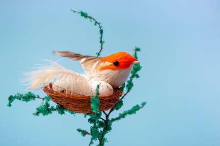 On a decorative tree, a nest with eggs and a small yellow bird on a blue background close up with copy spaceの写真素材