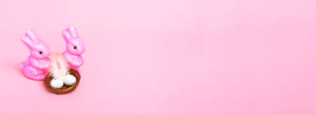 Easter bunnies and a nest with eggs on a pink background. Holiday concept. Close up copy space. Bannerの写真素材
