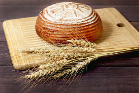 Freshly baked bread and ears of rye lie on a wooden board. Harvestの写真素材