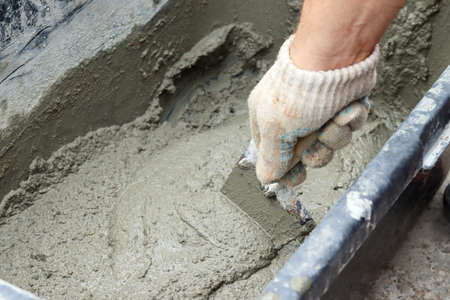 Mixing concrete by hand. Scooping up the concrete mixture with a trowelの写真素材