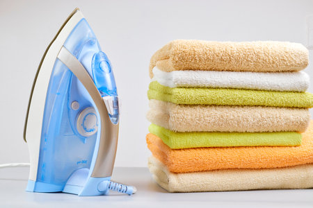 Pile of clothes and electric iron on the table on a light background. close-up of ironing tool and towels. good qualityの写真素材