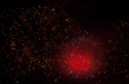 Red heart-shaped sparks of salute, orange, neon and golden sparks of fireworks in the sky and smoke...