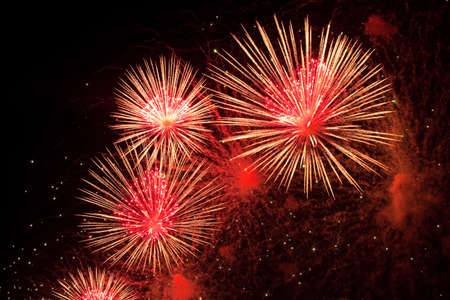 Red, pink and golden sparks of fireworks exploding in the sky and smoke from the charges. suitable...