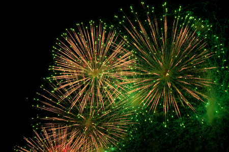Red, green and golden sparks of fireworks exploding in the sky and smoke from the chargesの写真素材
