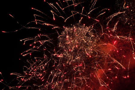 Red and golden sparks of fireworks exploding in the sky and smoke from the charges