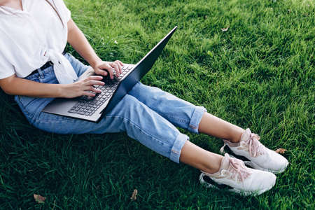 student girl with laptop outdoors sitting on the grass, surfing the internet or preparing for exams. Technology, education and remote work concept. Soft selective focus.の写真素材
