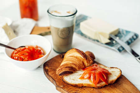 Breakfast with a fresh croissant and a cup of aromatic coffee latte, tangerine jam, butter and brie...