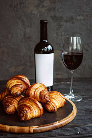 Freshly baked fragrant croissants on a dark stone board, a glass of red wine and a bottle. Romantic dinner.の写真素材