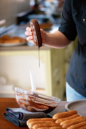 The pastry chef prepares a dessert. French eclairs or profiteroles from dark chocolate with glaze. Cakes with cream and topping. Soft selective focus.の写真素材