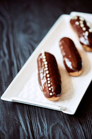 French dessert eclairs or profiteroles with dark chocolate glaze and drops. Pastry cakes with cream...