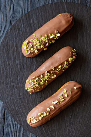 French dessert eclairs or profiteroles with milk chocolate glaze and pistachios on a black stone...