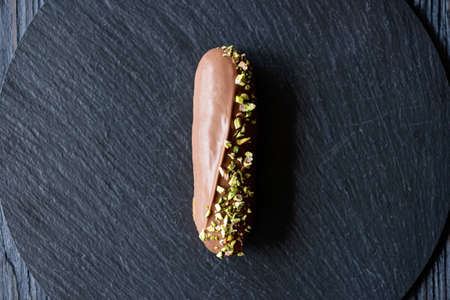 French dessert eclairs or profiteroles with milk chocolate glaze and pistachios on a black stone plate. Cakes with cream and topping. Soft selective focus.の写真素材