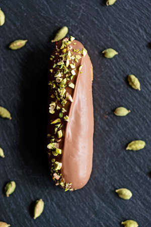 French dessert eclairs or profiteroles with milk chocolate glaze flavored with cardamom and pistachios. Cakes with pistachio cream and topping. Soft selective focus.の写真素材