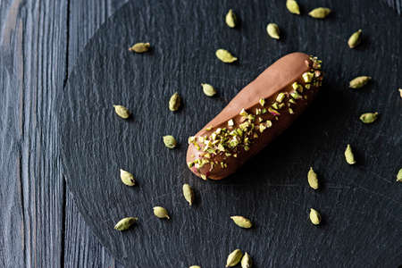 French dessert eclairs or profiteroles with milk chocolate glaze flavored with cardamom and pistachios. Cakes with pistachio cream and topping. Soft selective focus.の写真素材