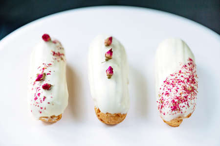 French dessert eclairs or profiteroles with rose-flavored white chocolate glaze, on a white...