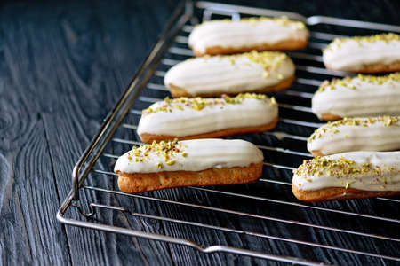 French dessert eclairs or profiteroles with white chocolate glaze with pistachios, on a pastry rack....