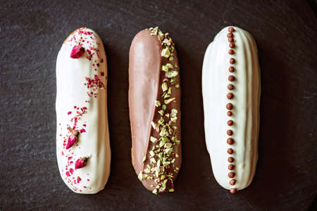 French dessert eclairs or profiteroles with chocolate icing and different toppings on a black stone...