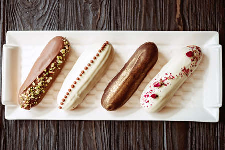 French dessert eclairs or profiteroles with chocolate glaze, with different toppings on a white...