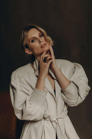 Fashionable portrait of a stylish blonde woman in elegant totall beige look leather trench coat and smoky eyes makeup in the studio. Spring - autumn fashion concept. Soft selective focus.の写真素材